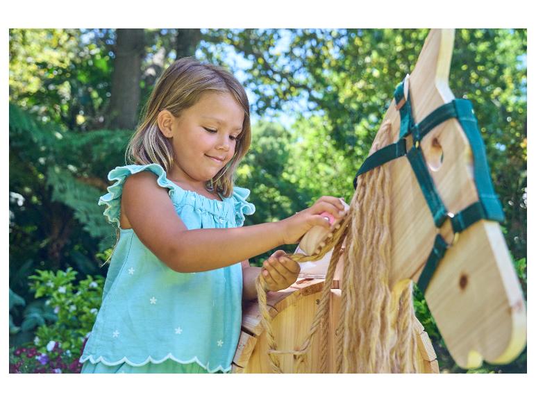 Une petite fille joue avec un cheval en bois dans le jardin.