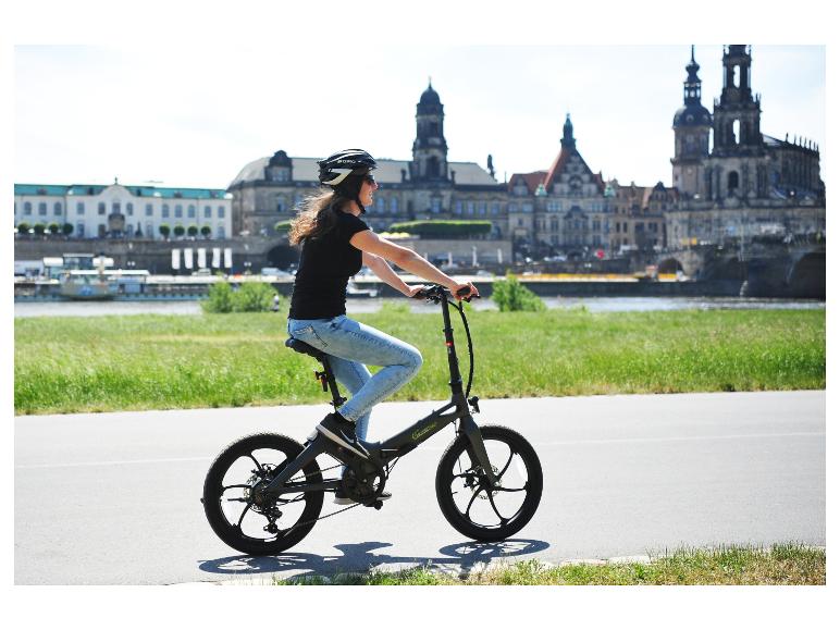 Femme à vélo électrique Sachsengrad sur une promenade au bord de l'eau avec un paysage urbain.