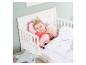 Enfant souriant dans un lit bébé avec parure de lit Peppa Pig et oreiller en peluche.