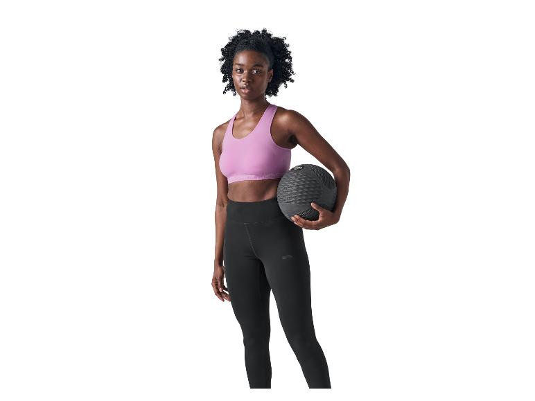Femme en brassière de sport rose et legging noir tenant un medecine ball.