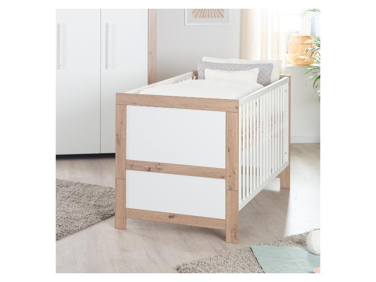 Lit bébé blanc et en bois avec literie dans une chambre d'enfant lumineuse.