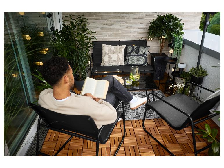 Homme lisant sur un balcon avec mobilier de jardin noir, plantes et lumières décoratives.