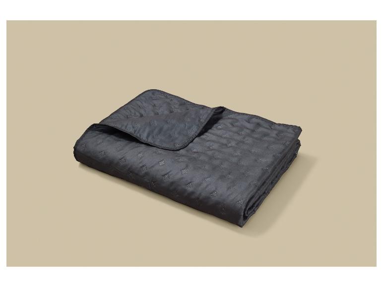 Couverture matelassée gris foncé pliée avec un motif floral subtil sur fond beige