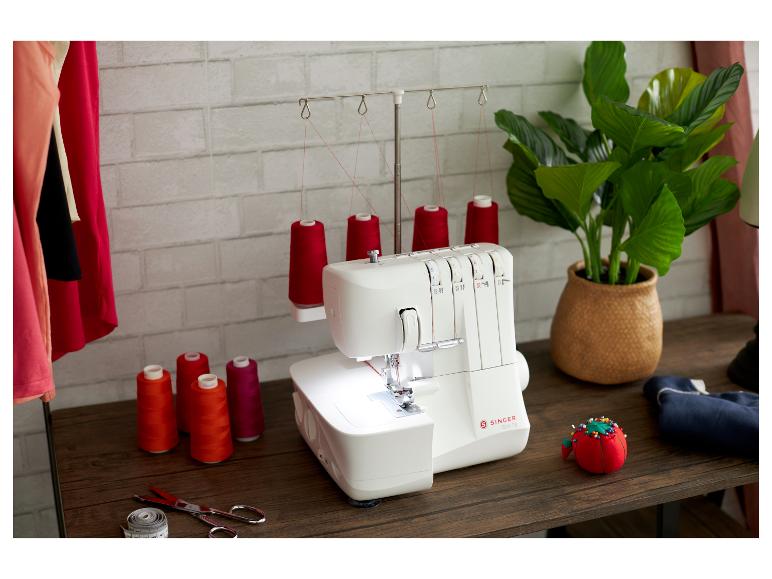 Machine à coudre blanche avec fils rouges sur une table en bois, à côté d'une plante et d'accessoires.