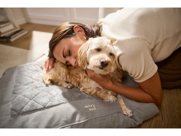 Une femme enlace son chien couché sur un panier gris avec texte brodé.
