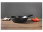 Une poêle wok noire sur une table en bois avec des tomates et des champignons.