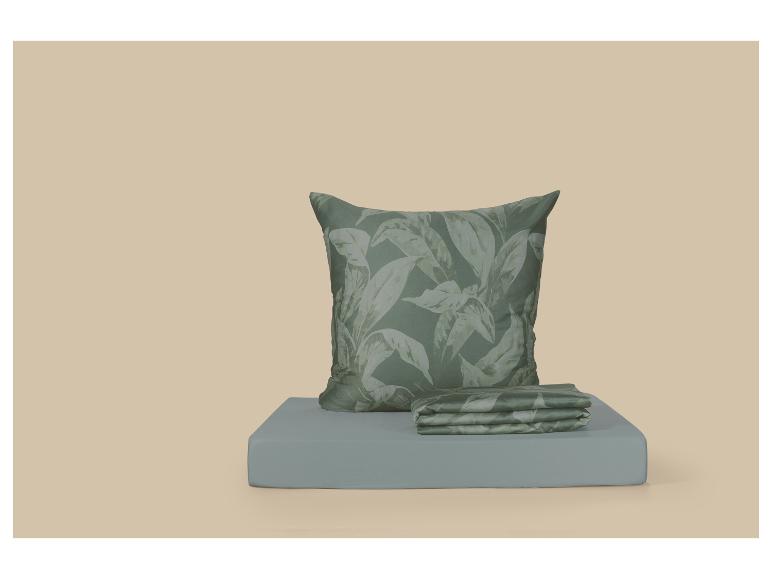 Coussin vert et linge de lit plié à motif de feuilles sur une surface bleu clair.