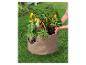 Une personne plante des poivrons et des herbes dans un sac de culture.