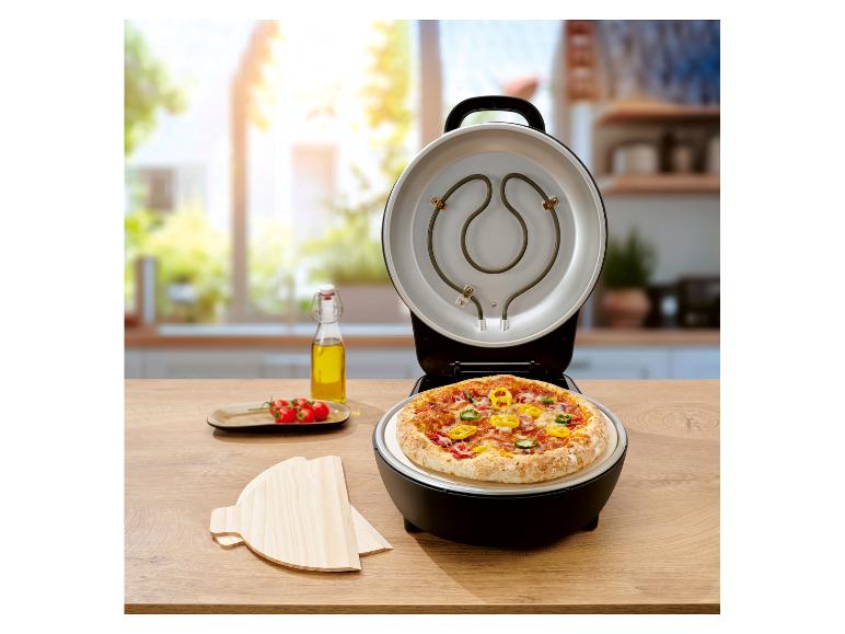 Four à pizza avec couvercle ouvert, pizza cuite à l'intérieur, huile et tomates sur une table en bois.