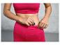 Une femme en brassière de sport et leggings roses glisse une clé dans sa poche.