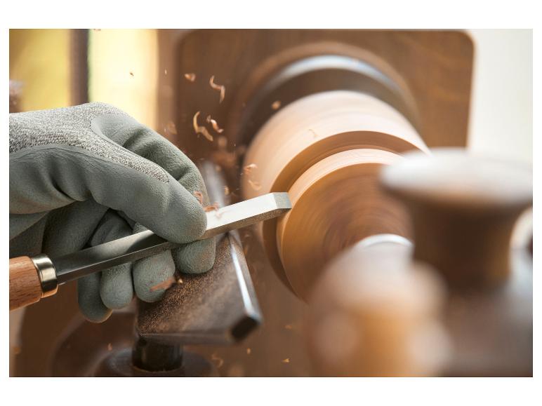 Une main gantée utilise un ciseau pour travailler un disque de bois sur un tour.