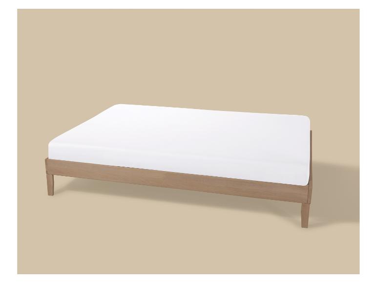 Lit en bois avec matelas blanc sur fond beige.