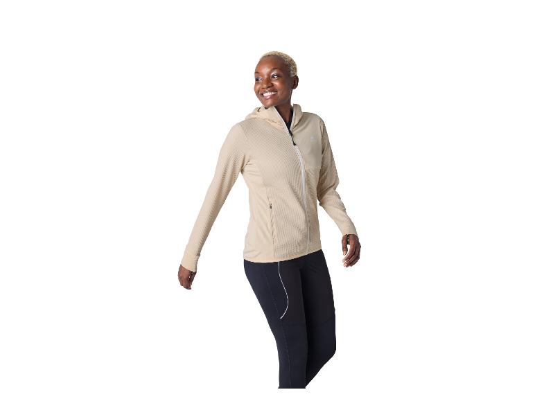 Femme souriante portant une veste de sport beige à capuche et un legging de sport noir.