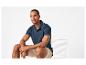 Homme en polo bleu marine et short beige assis sur une chaise blanche.