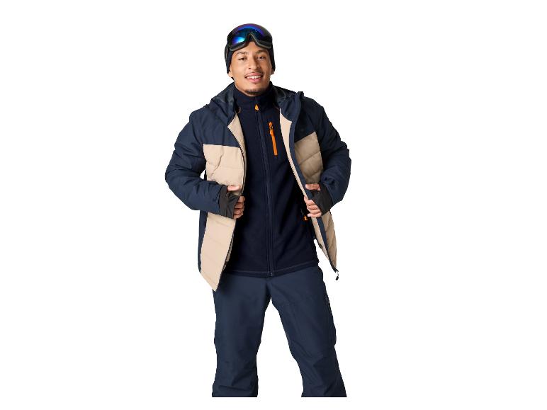 Homme en veste de ski bleu foncé et beige, pantalon et lunettes.
