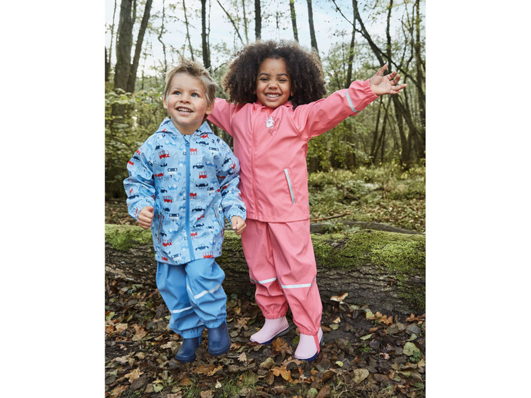 Deux enfants en vêtements de pluie, un garçon avec une veste bleue à motifs de voitures et une fille avec une veste rose.