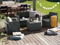 Un salon de jardin en osier gris avec une table basse sur une terrasse en bois.
