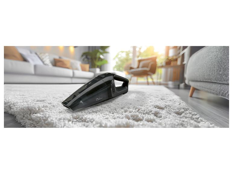 Aspirateur à main noir sur un tapis blanc, dans un salon lumineux.