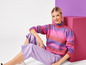 Une femme portant un pull rose à rayures et un pantalon violet.