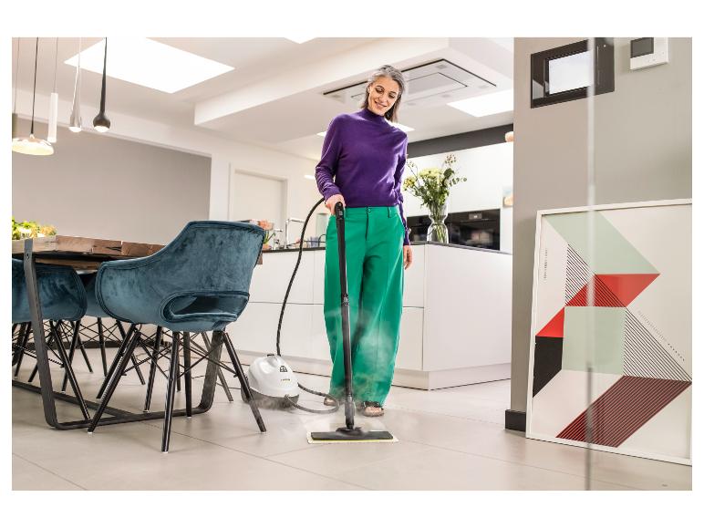 Femme nettoyant à la vapeur un sol carrelé dans une cuisine-salle à manger moderne.