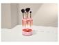 Nettoyeur de pinceaux de maquillage rose avec quatre pinceaux, sur une surface blanche avec un fond clair.