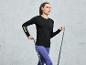 Une femme en tenue de sport noire à manches longues portant l'inscription 'Break the Limits', s'entraînant avec un élastique de résistance.