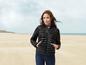 Une femme portant une veste matelassée noire sur la plage.