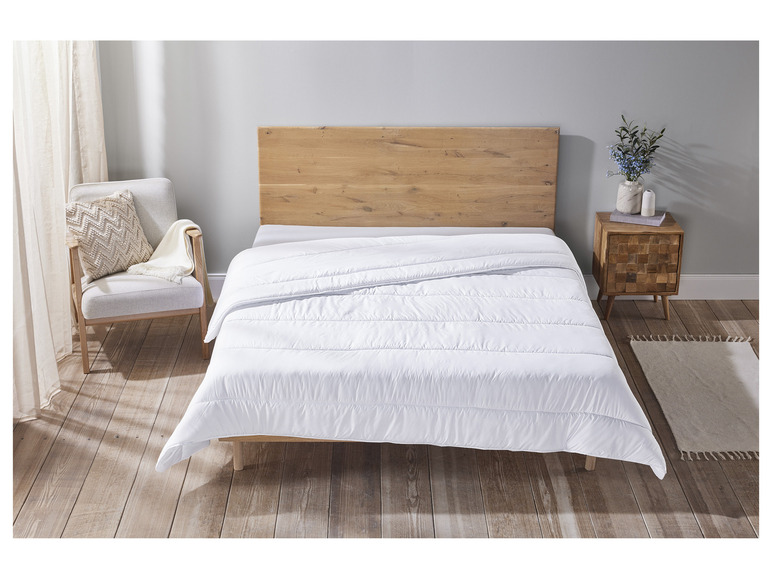 Une couette blanche sur un lit en bois avec une table de chevet et une chaise.