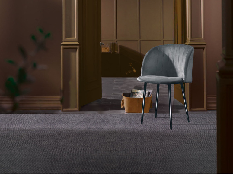 Une chaise en velours gris avec des pieds noirs sur un tapis gris.