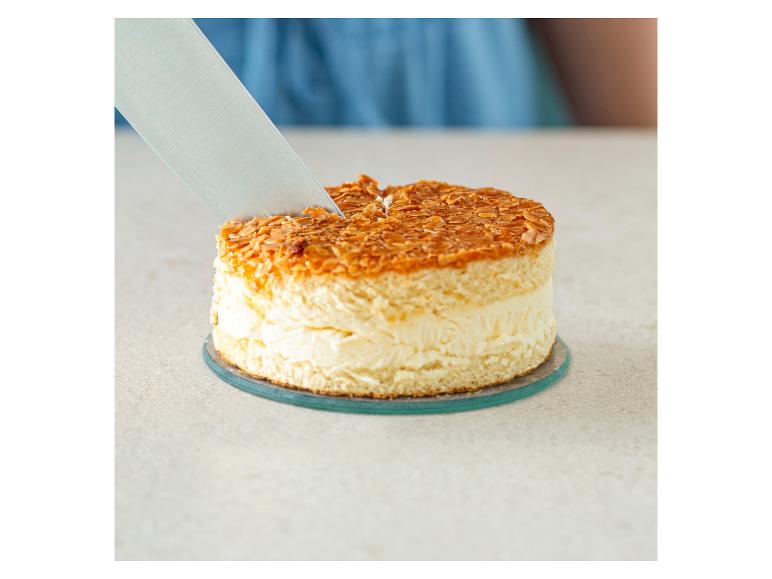 Un couteau coupe un gâteau rond avec une garniture d'amandes.