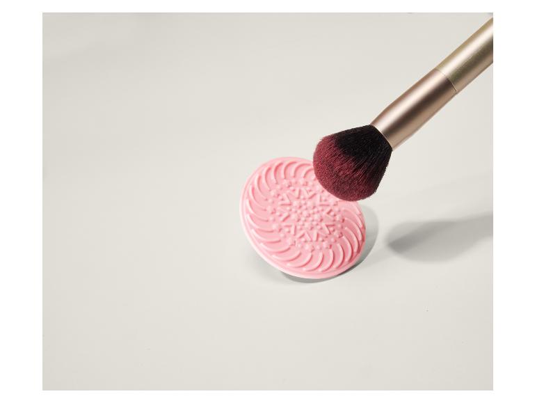 Un tapis de nettoyage rose pour pinceaux de maquillage avec un pinceau dessus.