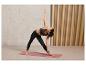Une femme en brassière de sport et leggings fait du yoga sur un tapis rose.