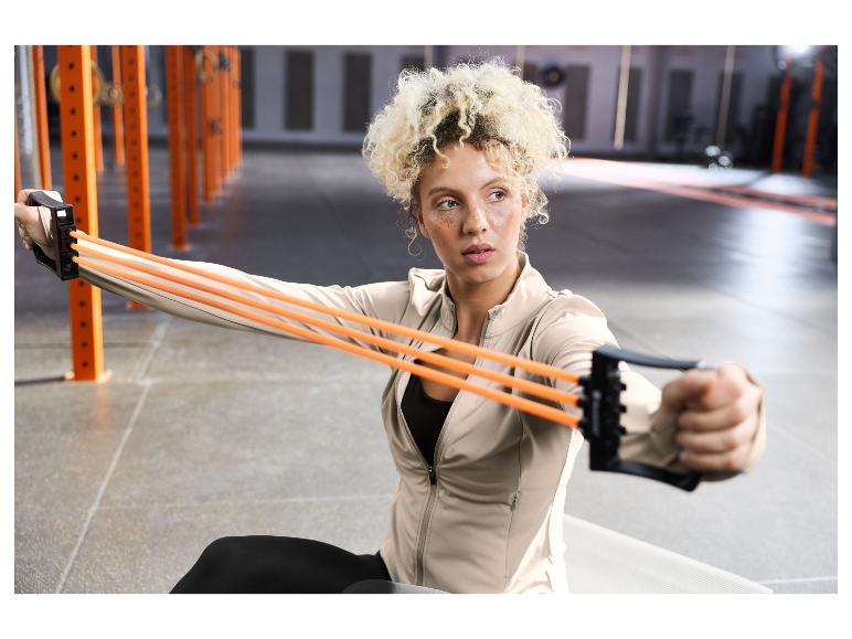 Femme aux cheveux bouclés s'entraînant avec des bandes de résistance oranges dans une salle de sport.