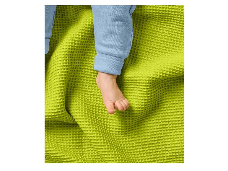 Pied de bébé en pyjama bleu sur une couverture gaufrée verte.