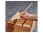 Main appliquant du vernis sur une caisse en bois avec un pinceau, sur un fond gris.