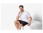 T-shirt blanc et short noir pour homme, assis sur un pouf.
