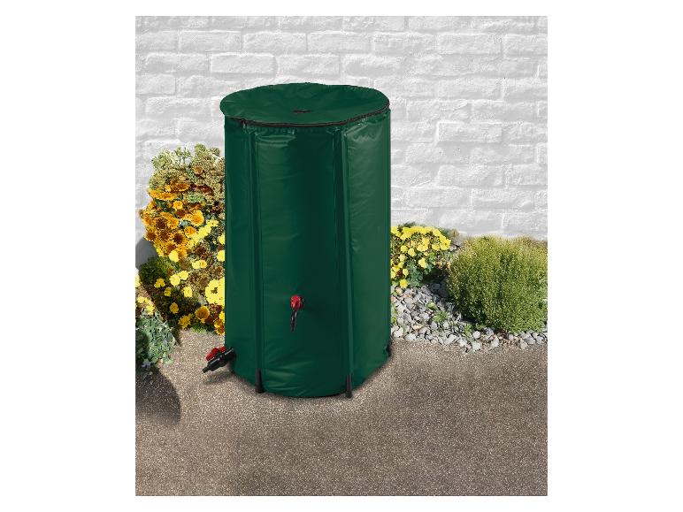 Tonneau à eau de pluie vert avec robinet, placé à l'extérieur près d'un mur de briques blanches et de fleurs.