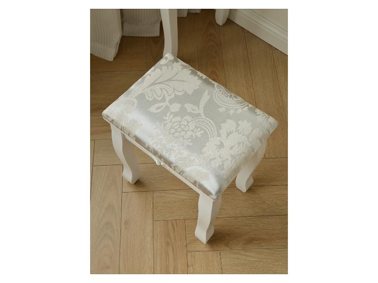 Tabouret de coiffeuse blanc avec assise à motif floral gris clair sur un parquet.