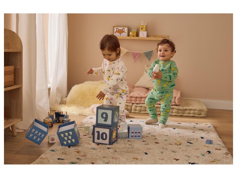 Deux jeunes enfants en pyjama animalier, jouant avec des blocs et un train en bois sur un tapis.