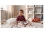 Bébé en body bordeaux et pantalon beige, assis sur une couverture avec un livre.