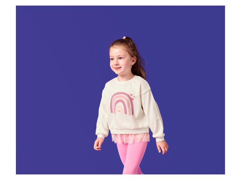 Fille en sweat-shirt crème imprimé arc-en-ciel et leggings roses.