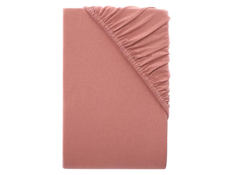 Un drap-housse rose poudré est présenté plié sur un fond blanc.