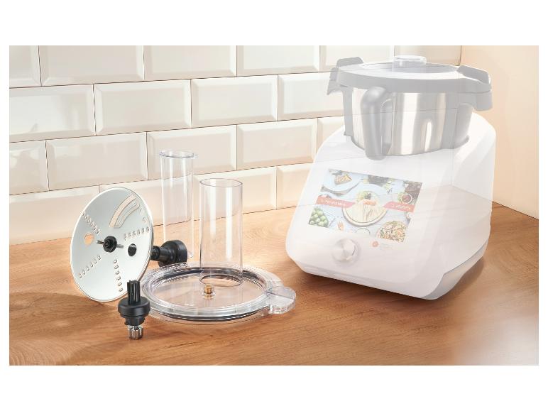 Robot culinaire avec accessoires sur un comptoir en bois devant un mur carrelé.