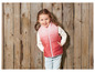 Une fille porte un gilet rose et un pull blanc devant un fond en bois.
