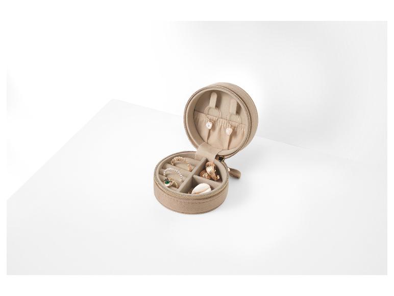 Une boîte à bijoux beige avec des boucles d'oreilles, des bagues et un collier dorés.