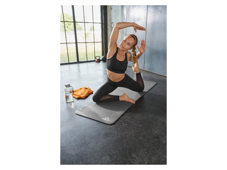 Femme faisant du yoga sur un tapis, avec une bouteille d'eau et une serviette.