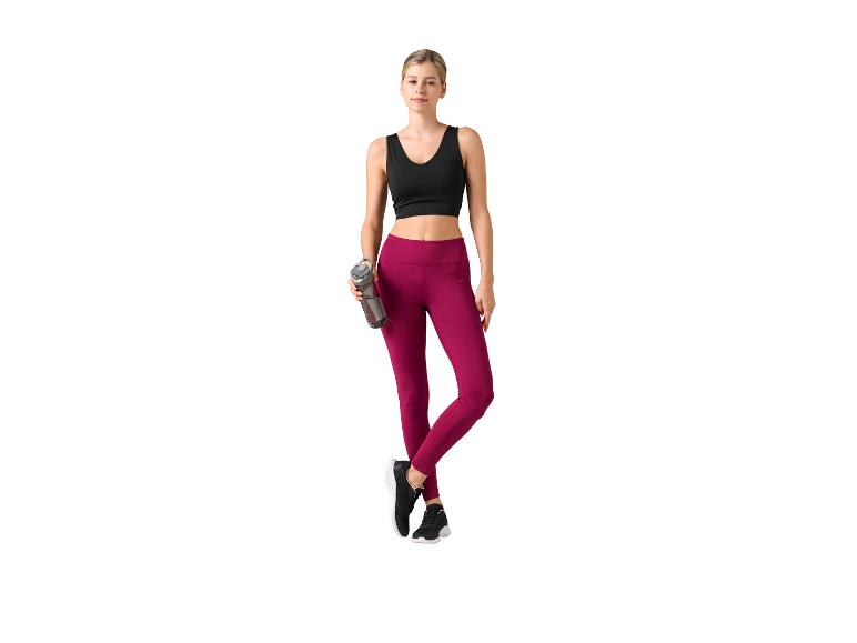 Femme en brassière de sport noire et legging bordeaux, tenant une bouteille d'eau.