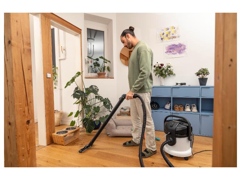 Homme aspirant un parquet avec un aspirateur eau et poussière, à côté de gamelles pour animaux.