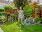 Une femme marche avec une tondeuse à gazon robotisée dans un jardin.