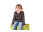 Enfant souriant en pull et jean assis sur un tabouret vert.